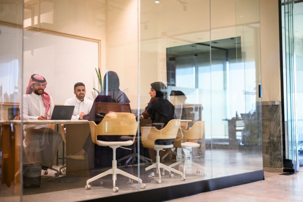 Wide shot of Saudi Arabian business team in traditional dressing having meeting inside glass walled contemporary office